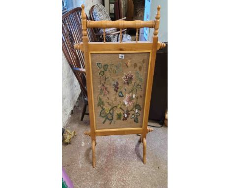 A blonde wood framed fire screen with central embroidered floral panel under glass