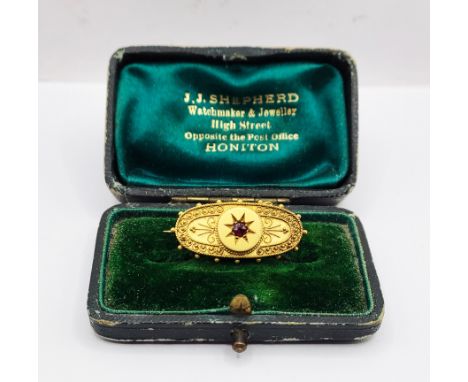 A cased late Victorian 18ct. gold ornate oval panel brooch, set with central ruby