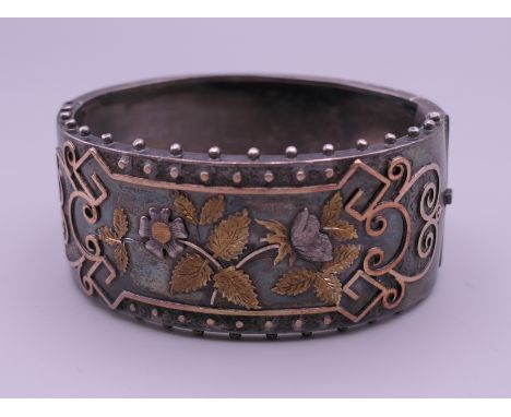 A Victorian white metal (silver) and two colour yellow metal (gold) bangle. 6 cm wide, 4.5 cm deep.  42.4 grammes total weigh