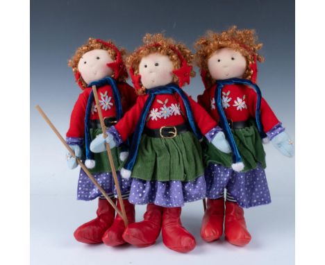 A trio of identical dolls with red curly hair, fashioned for the holidays with a green, red and purple dress, red star shaped