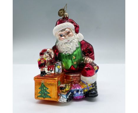 Features a glittery winking seated Santa Claus painting a nutcracker, surrounded by toys. Glitter and gilded details. Issued: