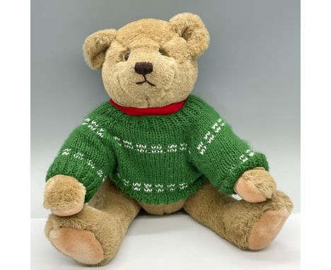 Features a precious teddy wearing a red and green sweater. Gund label. Issued: 1982Dimensions: 13"L x 9"W x 15.5"HManufacture