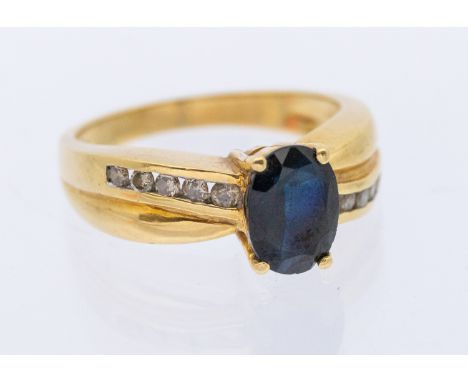 A sapphire and diamond 18ct gold cross over ring, set with an oval mixed cut sapphire approx 7x4mm, claw set to a channel set