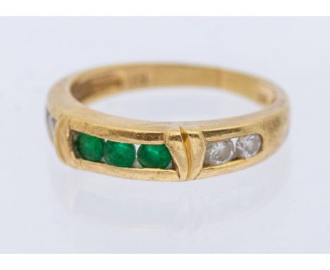 An emerald and diamond ring, comprising a central channel set row or three round mixed cut emeralds, with two round brilliant