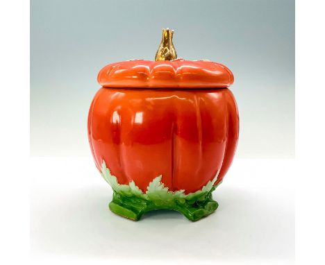 An orange ceramic pumpkin jar with a detachable lid that has a gold-colored stem and is sitting on top of four legs that are 