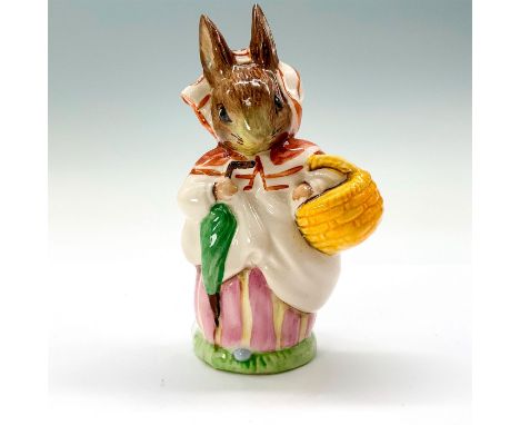 A figurine of Mrs Rabbit wearing a white and red bonnet and a yellow and pink dress while holding a picnic basket and umbrell