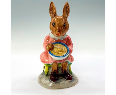 A figurine of a brown bunny wearing a light red dress while preparing a mixture in a bowl. Royal Doulton backstamp. Dimension