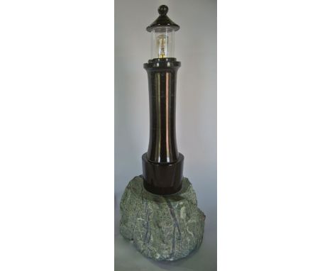 A desk lamp in the form of a lighthouse, crafted from polished deep red serpentine upon a rocky setting in worked grey serpen