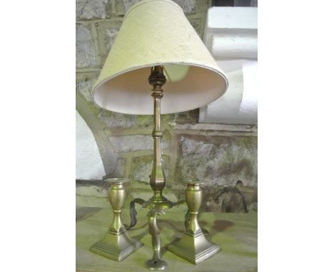 A brass student's lamp raised on scrolling tripod supports, together with a short pair of brass candlesticks with simple inci