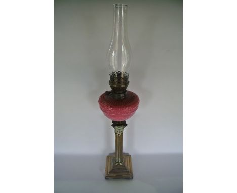 A good quality Victorian oil lamp with opaque cranberry glass font above a fluted column support with ornate embossed Corinth