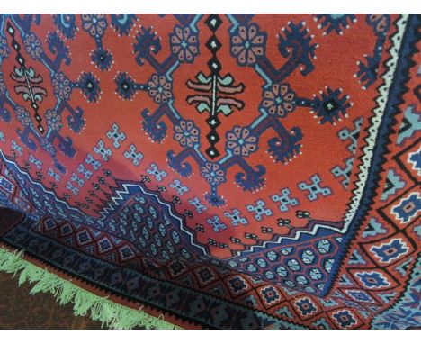 A wool carpet in the Persian style with red field and abstract floral detail within geometric borders 320 x 200 cms