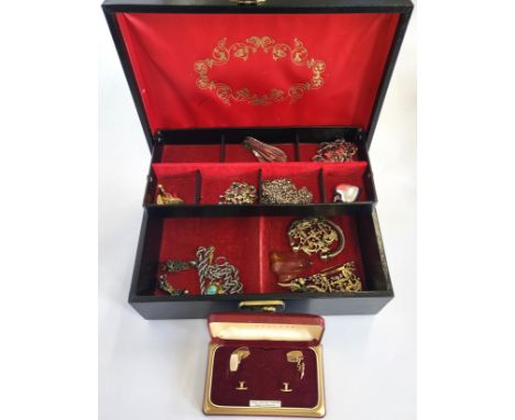 A black hinge lid jewellery box containing amber, buckles, chains, a slave bangle, a glass pendant, and a boxed set of engine
