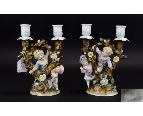 Conta and Boehme Pair of Double Candlesticks, each showing two children playing amongst trees, the older girl teamed with a y