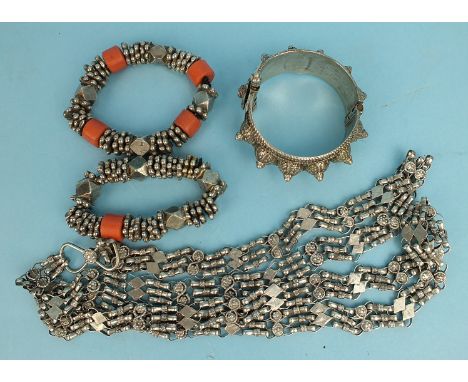 An Omani silver hinged bangle with raised decoration, two Omani silver bracelets of beaded disks with coral beads and a long 