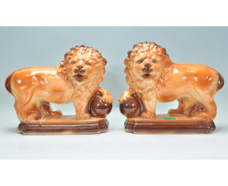 A matching pair of early 20th Century Staffordshire ceramic fire dogs in the form of lions having glass eyes with their paws 