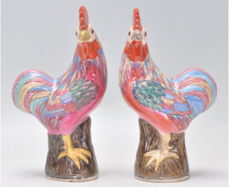 A pair of 20th Century Chinese ceramic cockerel figurines having polychrome glazed feathers, each modelled perched on a log w