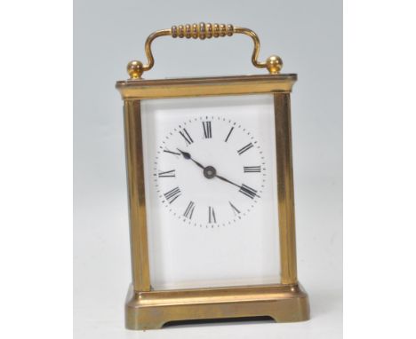 An English 20th century brass carriage clock having scrolled handle to the top with open window escapement. The enamel face w