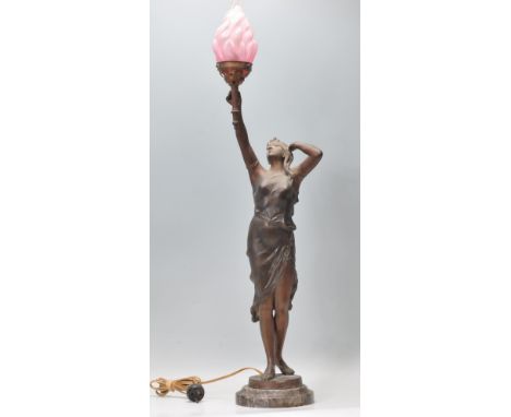 An early 20th Century Art Nouveau table lamp in the form of a female figure holding a torch aloft, having a pink glass flame 