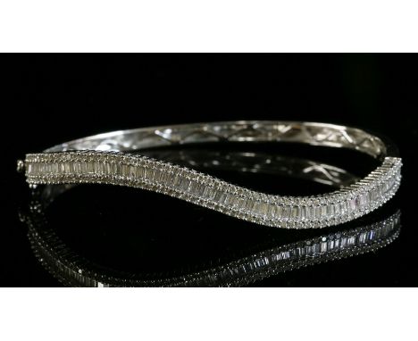 An 18ct white gold, diamond set, hinged bangle,with a wave-shaped top half.  A central row of baguette cut diamonds, with two