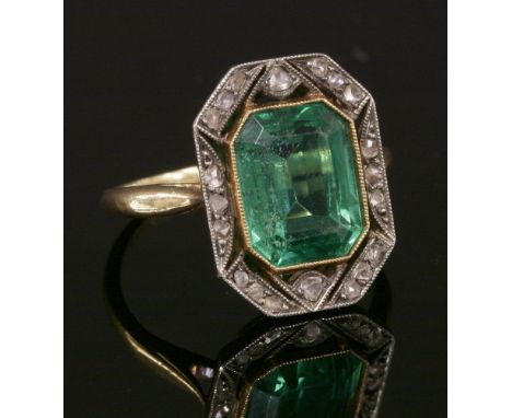 An Art Deco green paste and diamond cluster ring,with an emerald cut green paste, milligrain set to a plain collet, a pierced