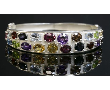 A silver gem set hinged bangle,with a shallow 'D' section top half with assorted gemstones to include, garnets, citrines, ame