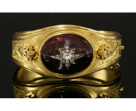 A Victorian gold garnet and diamond hinged bangle,with a central oval cabochon garnet with applied graduated diamond set star