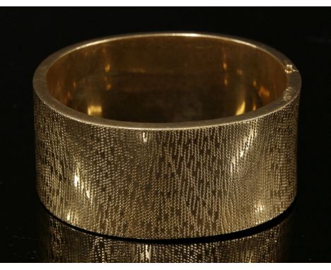 An Austrian oval hinged bangle, c.1960,of slightly concave form, with fine textured decoration.  A concealed box clasp with A