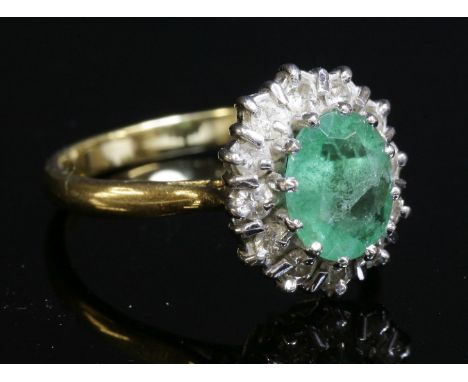 An emerald and diamond oval cluster ring, with an oval mixed cut emerald, claw set to the centre.  A border of brilliant cut 