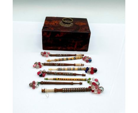 A burlwood hinged lidded box with molded brass medallion and ring handle on top. The box contains 8 carved and metal inlaid l