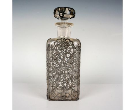 A clear glass vanity bottle with stopper, wrapped in a silver-tone metal floral case. CLC Co. embossed on the base. Dimension