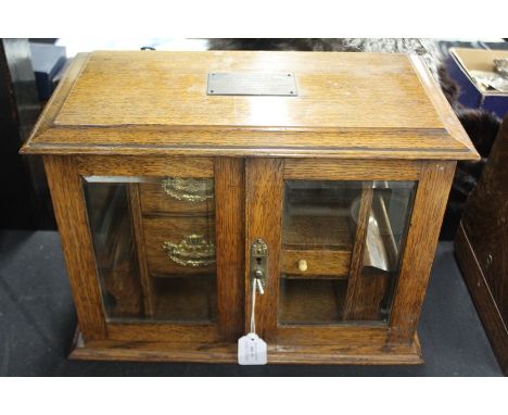 Edwardian oak smokers cabinet, the bevelled glazed doors opening to reveal three drawers, two open recesses and two sliding p