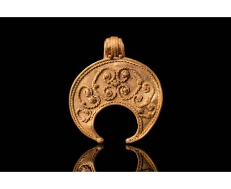 Ca. 300 - 100 BC. A gold lunula pendant with scrollwork decoration. The crescent-shaped body is framed by a twisted wire bord