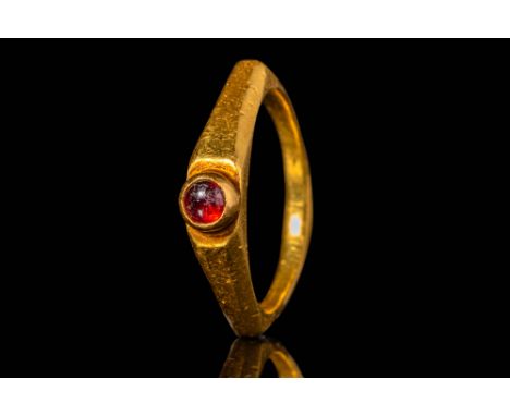 Ca. AD 300 . A gold ring set with a garnet cabochon in a raised circular bezel. The hoop of the ring is slender and faceted, 