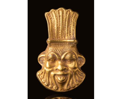 Late Period, Ca. 664 - 332 BC.A gold pendant in the form of the head of the god Bes, with a broad face framed by a stylised b