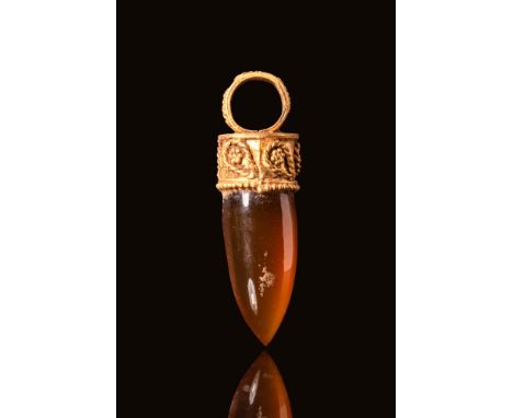 Ca. 300 BC. A gold pendant featuring a tooth-shaped carnelian stone set within an ornate gold cap. The carnelian is smoothly 
