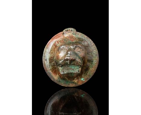 Ca. AD 200 - 300. A circular bronze phalera featuring a lion’s head in high relief. The face is framed by a thick, wavy mane 