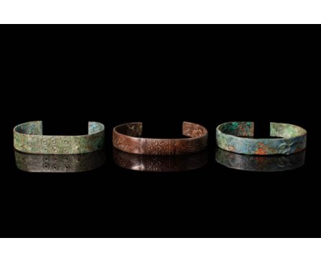 Ca. 800 - 1100 BC. A collection of three bronze bracelets, each with a flat, open-ended band of uniform width. The first brac