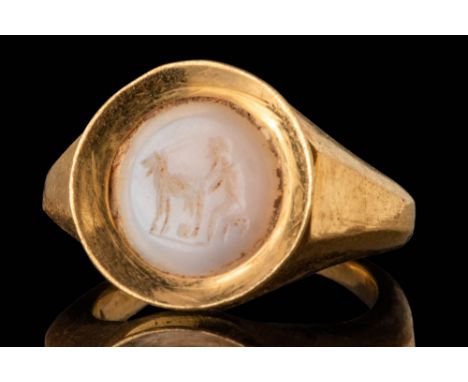 Ca. AD 300. A chalcedony intaglio engraved with a scene of a seated satyr milking a goat. The figure faces left, seated on a 