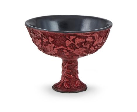 A Chinese cinnabar lacquer stem cup, late Ming dynasty, carved with flowering peony and flowering cherry against a diaper gro