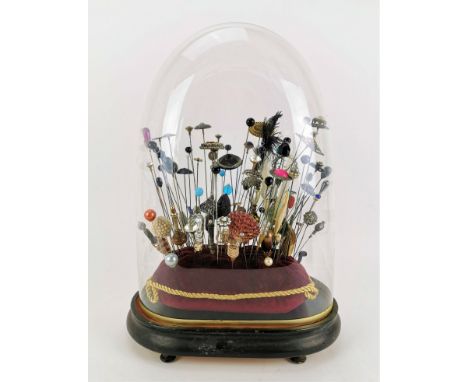 A collection of late Victorian and Edwardian hatpins under a shaped dome, the pins held in a red velvet cushion with gilt tri