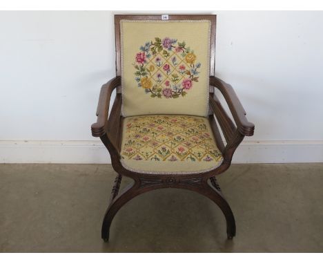 A circa 1900's oak X framed armchair with needlepoint upholstery on hidden castors
