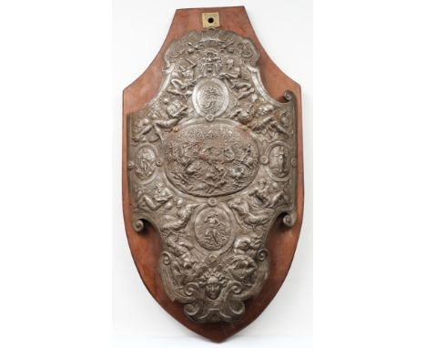 A steel shield-shaped plaque: decorated with neo-classical warriors, grotesque masks and serpents, mounted on a polished wood