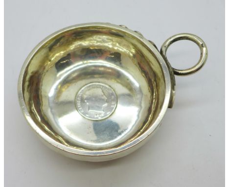 A continental white metal wine taster with snake handle, inset with a silver coin dated 1812 