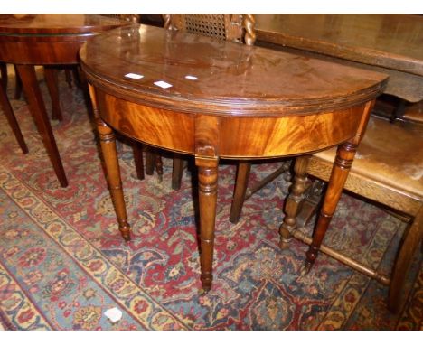 A Regency mahogany fold-over card table of demi lune form raised on turned and ringed tapering legs to brass caps and castors