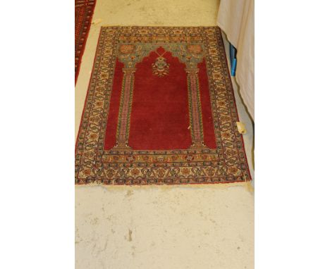 A Persian Prayer rug with architectural style column decoration to the centre field on a red ground within a cream ground scr