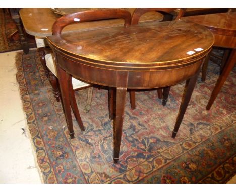 An early 19th Century mahogany tea table of demi-lune form, the fold-over top satinwood strung over a plain frieze on square 