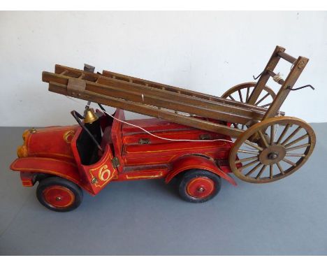 A large custom-built wooden model of a vintage fire engine; extendable ladders and red-painted coachwork body after the origi