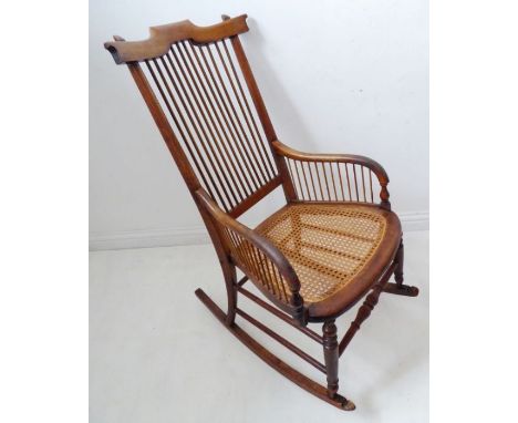 A late 19th century American-style walnut rocking chair; comb-style back above a rattan-cane seat with turned legs united by 