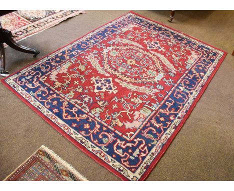 Indian Rug, the blood red field centered by a serrated panel enclosed by indigo borders, 207cm by 153cm; together with two "B