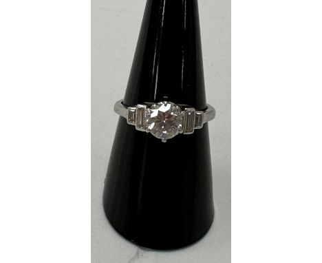 A solitaire diamond ring, the central brilliant cut stone 1 carat flanked by two small emerald cut diamonds to the shoulders 